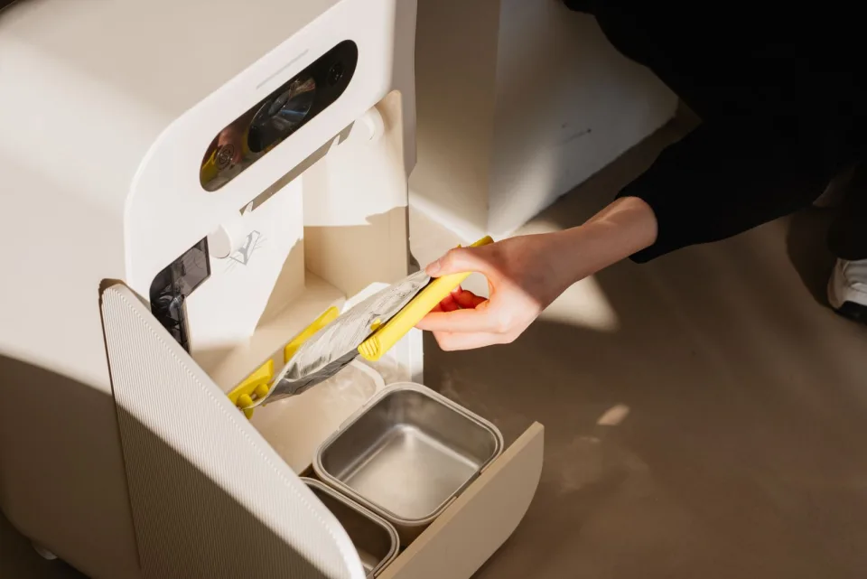 Main remplissant le tiroir du robot Yomy avec un sachet de recharge croquettes